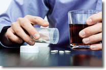 Person with glass of alcohol and pills on table